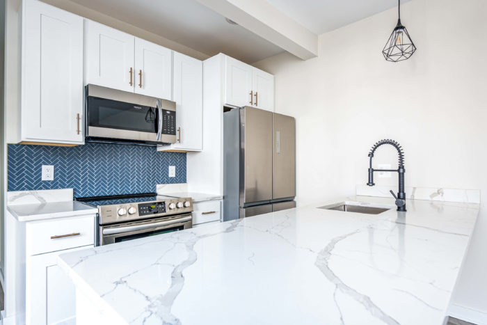 a white kitchen with blue backsplash and stainless steel appliances